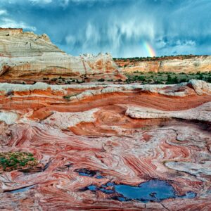 A colorful desert scene depicts red rocks in the foreground, with a stormy sky and a small rainbow in the background.