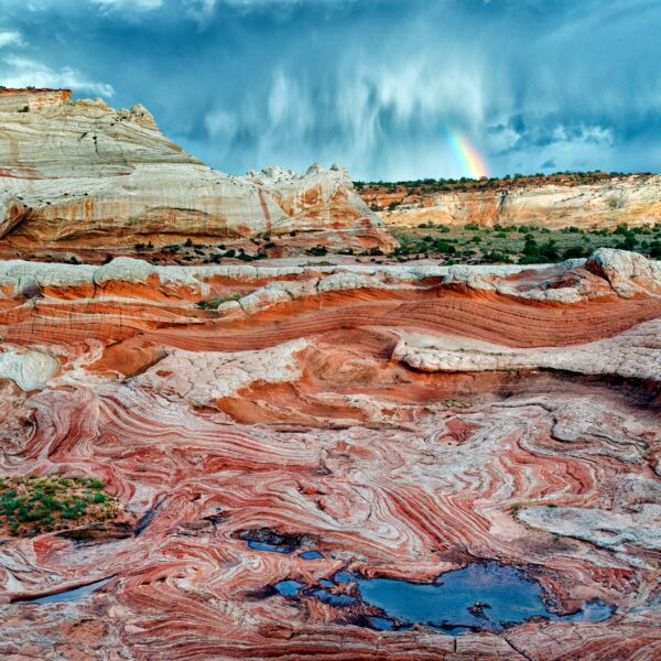 A colorful desert scene depicts red rocks in the foreground, with a stormy sky and a small rainbow in the background.