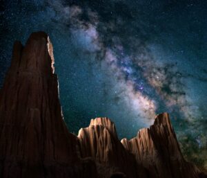The milky way galaxy can be seen behind three distinct mountain peaks in this night shot.