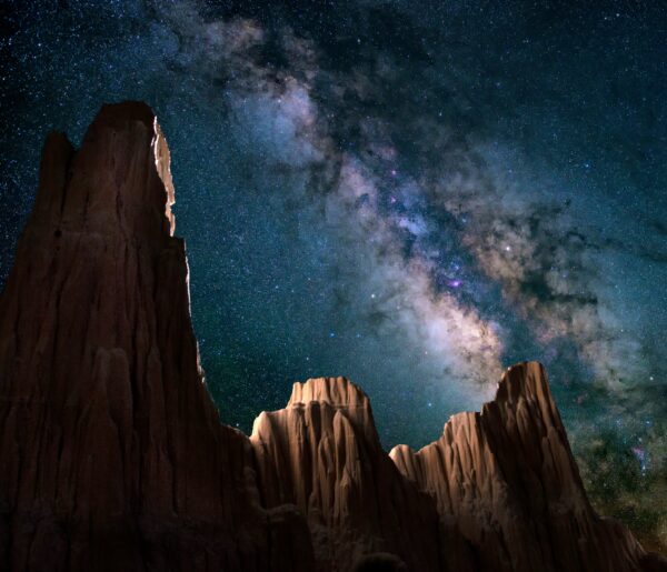 The milky way galaxy can be seen behind three distinct mountain peaks in this night shot.