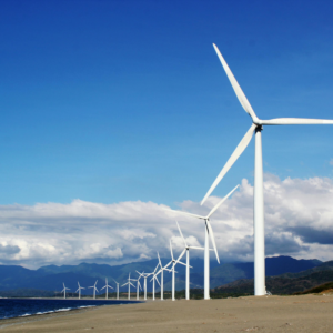 Row of windmills against a blue sky with clouds just above a mountain range.