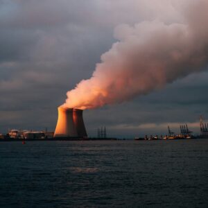 A power plant in the distance emits plumes of water vapor. In the foreground is a body of water.