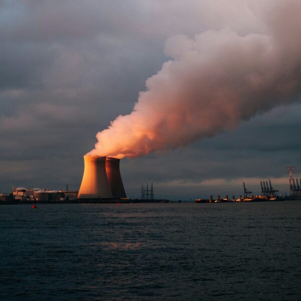 A power plant in the distance emits plumes of water vapor. In the foreground is a body of water.