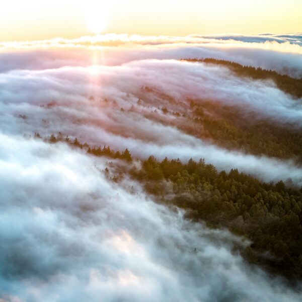 Fog rolls over mountains as the sun sets in the background.