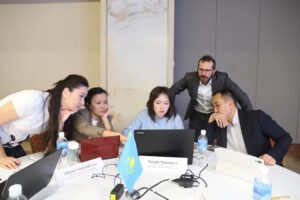 A group of professionals look at a laptop as an instructor leans in from behind during a workshop.