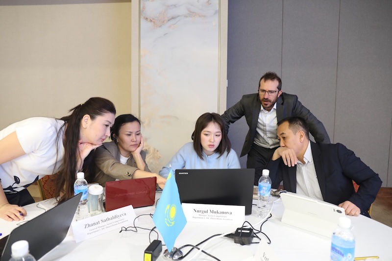 A group of professionals look at a laptop as an instructor leans in from behind during a workshop.