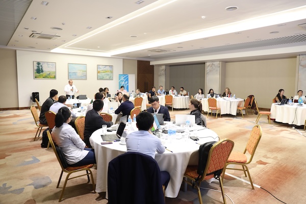A room is filled with round tables and participants in a workshop.